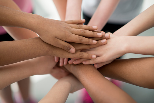 A multi-ethnic group of elementary age children are holding their hands together in huddle.