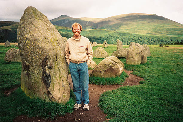 Tourist at Castlerigg stone circle, Lake District, England, ancient, mysterious A young, bearded man at the stone circle of Castlerigg near Keswick in the Lake District in England. The circle of standing stones is thought to be 5,000 years old. keswick photos stock pictures, royalty-free photos & images