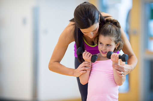 A mother is teaching her daughter how to lift weights at the gym.