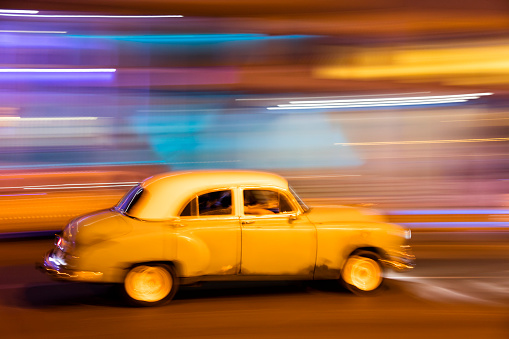 Vintage American car travels in motion blur through the dark streets of Havana, Cuba at night.