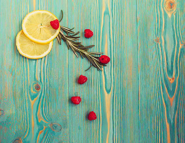 Lemon slices, raspberry and rosemary on turquoise colored wooden desk