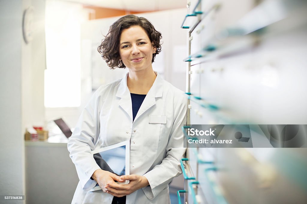 Pharmacist leaning to a medicine shelf with digital tablet Portrait of confident young female pharmacist leaning to a medicine shelf with a digital tablet Pharmacist Stock Photo