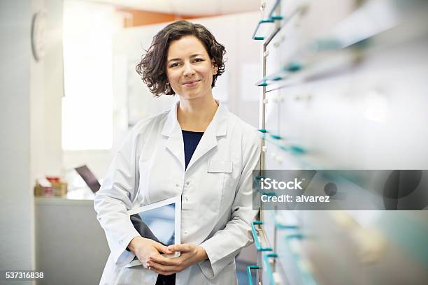 Pharmacist Leaning To A Medicine Shelf With Digital Tablet Stock Photo - Download Image Now