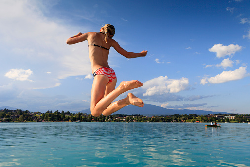 girl jumping in the Faakersee in Carinthia on a sunny day in summer; Egg am See, Austria