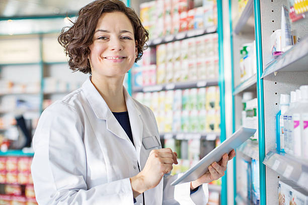 Female pharmacist with a digital tablet Female pharmacist with a digital tablet in drug store standing by medicine shelves online pharmacy stock pictures, royalty-free photos & images