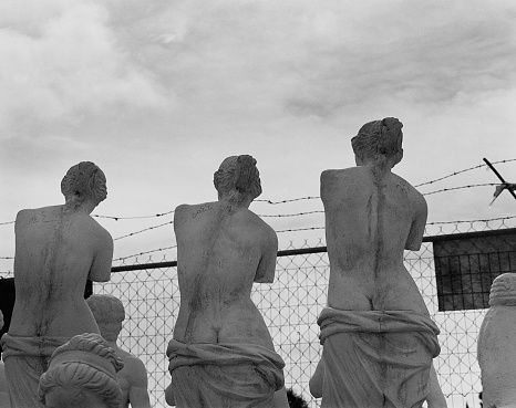 Three mass-produced, identical Venus De Milo statues for sale by the roadside. Black and white.
