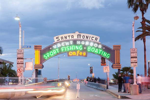 Santa Monica, USA - October 5, 2015;Neon entrance sign and arch to Route 66 west end Santa Monica Pier at night long exposure  blurring people Los Angeles,California, USA