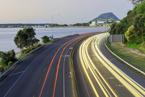 Highway lightstreams along Takitimu Drive at dusk looking north Highway lightstreams along Takitimu Drive at dusk looking north with Mount Maunganui on horizon. mount maunganui stock pictures, royalty-free photos & images