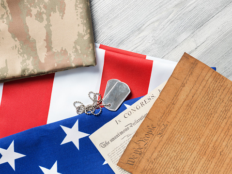 US constitution documents, dog tag, and camouflage clothes,American Flag on gray wooden floor.The objects are placed on the left side.Photo was shot in studio with a medium format camera Hasselblad H4D in studio and in horizontal composition.