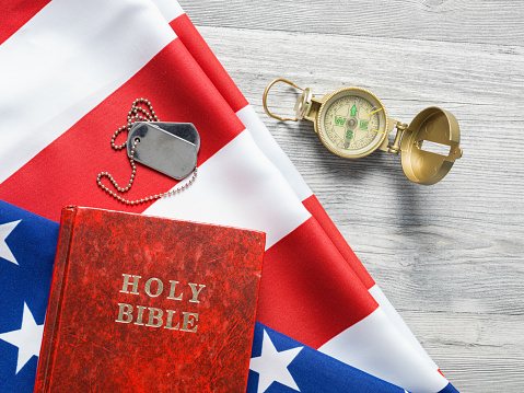 Bible,compass , dog tag, and American Flag on gray wooden floor.The objects are placed on the left side.Photo was shot in studio with a medium format camera Hasselblad H4D in studio and in horizontal composition.