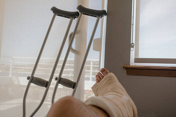 Injured Person With Sprained or Broken Ankle Foot Crutches Injured Person With Sprained or Broken Ankle or Foot Sits Inside With Crutches Looking Outside the Sliding Glass Door Window on a Sunny Day. ankle photos stock pictures, royalty-free photos & images