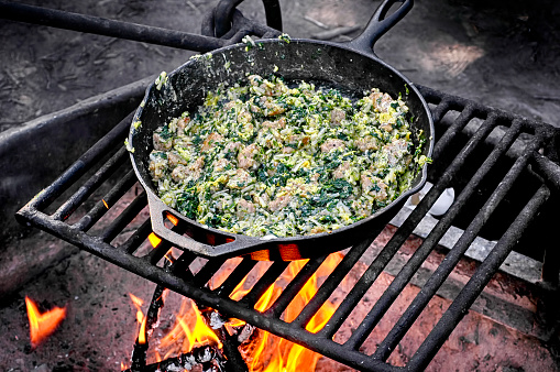 Sausage and spinach egg scramble cooked on a campfire in cast iron skillet