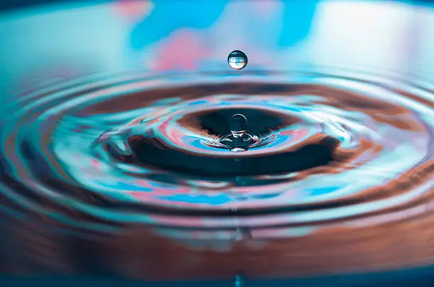Macro photo of water drops falling into a pool of water, causing a splash and ripples.