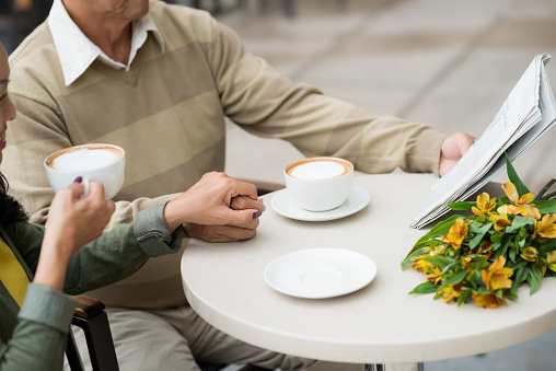 Cropped image of couple reading newspaper when sitting in cafe