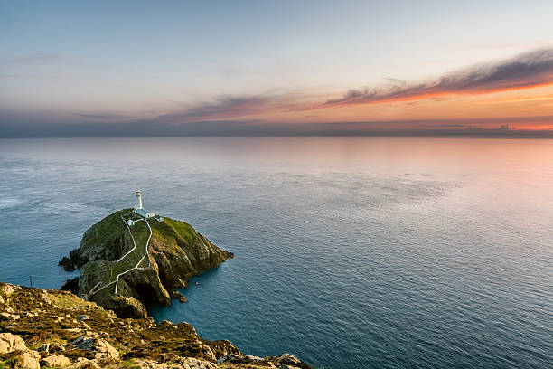 Lighthouse on a rock island with a beautiful orange sunset.
