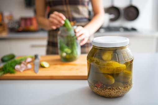 Closeup on jar of marinated cucumbers on table and housewife pickling in background