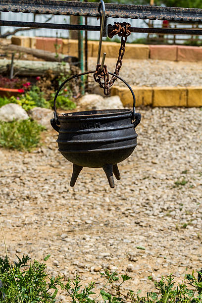 Old cast iron pot on a three legs, Israel Old cast iron pot on a three legs for cooking is suspended on the hook, on the farm in the desert, Israel three legged race stock pictures, royalty-free photos & images