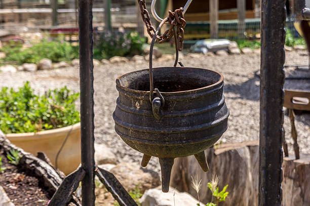 Old cast iron pot on a three legs, Israel Old cast iron pot on a three legs for cooking is suspended on the hook, on the farm in the desert, Israel three legged race stock pictures, royalty-free photos & images