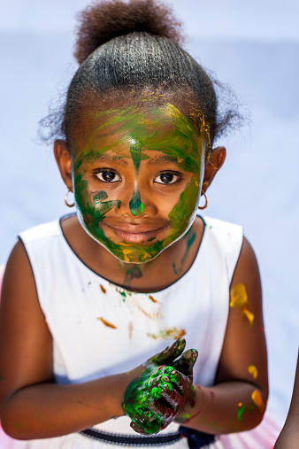 Close up portrait of cute African girl with painted face at painting session.Isolated against light background.