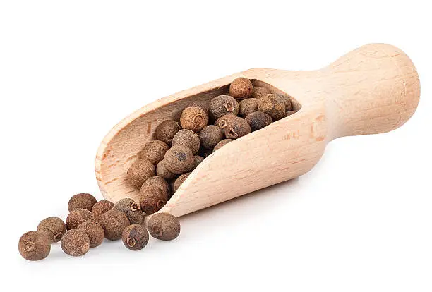 pimento peppercorns in wooden scoop isolated on white background. Whole allspice berries in wooden scoop. Myrtle pepper. Jamaica pepper. Spice of peppers in a wooden scoop
