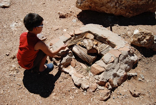 Boy crouching next to an ancient fireplace, located at the Grand Canyon, USA.