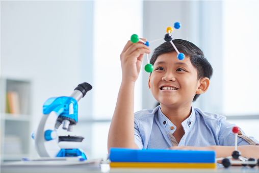 Happy schoolboy looking at molecular model in his hands