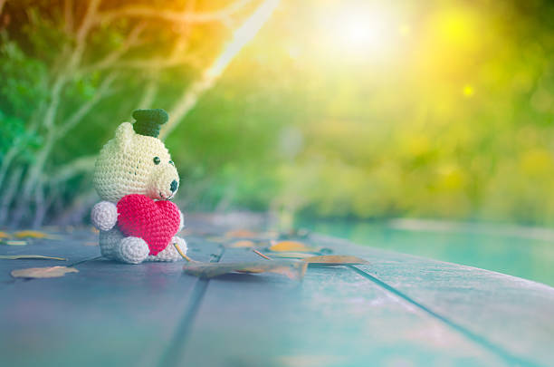 Teddy Bear with red heart sitting on wooden bridge in soft light. - Vintage tone