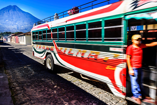 Antigua, Guatemala - October 5, 2014:  Fare collector looking for passengers on chicken bus known locally as a camioneta in Spanish colonial town & UNESCO World Heritage Site of Antigua. Agua volcano towers in the background.