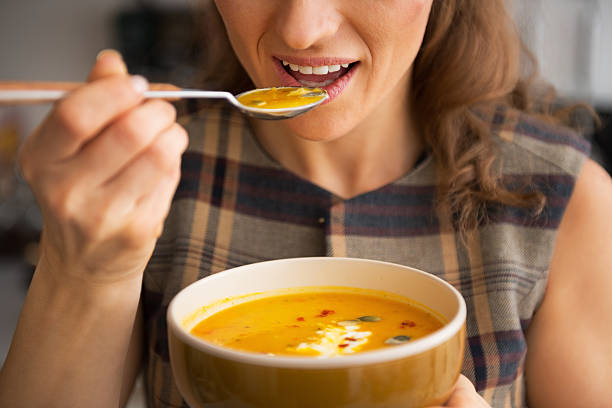 zbliżenie na młoda kobieta jedzenie zupa z dyni w kuchni - spoon heat pumpkin eating zdjęcia i obrazy z banku zdjęć