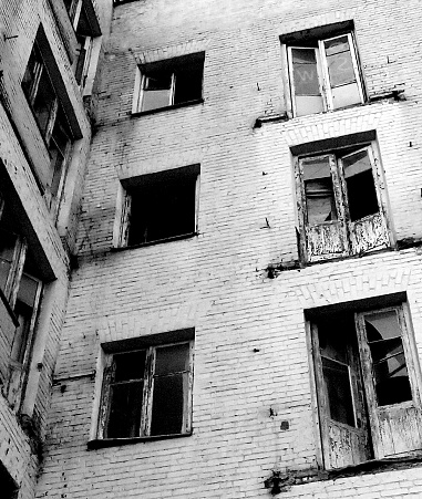 Old abandoned house. Windows and balconies with broken windows. Black and white photo. The house is brick.