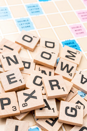 Miami, Florida, USA - June 22, 2014: Lettered wooden tiles mixed up on Scrabble game board. Scrabble is a fun and educational game distributed by Hasbro