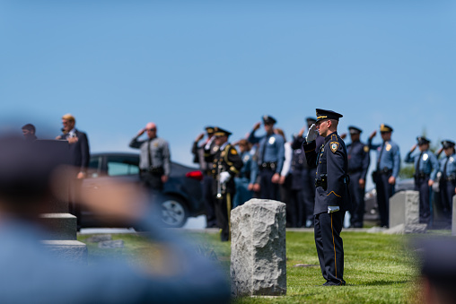 Weston, Missouri, USA - May 14, 2016: A funeral service for Detective Brad Lancaster, who was shot and killed on May 9, 2016, was held at Graceland Cemetery in Weston, MO., May 14,2016. A Lenexa, Kansas police officer stands saluting during a moment of silence at the grave site.
