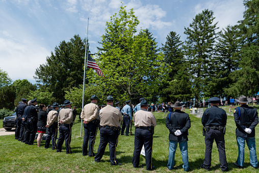 Weston, MO, USA - May 14, 2016: A funeral for Kansas City, Kansas Detective Brad Lancaster, who was shot and killed on May 9, 2016, was held at Graceland Cemetery, in Weston, MO., May 14, 2016. Platte County Sheriff's officers and other departments encircle a flag at half-mast while the family arrives.