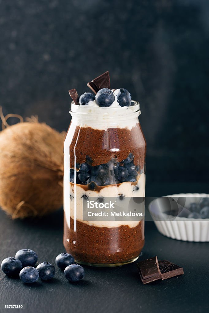 Chocolate chia pudding Healthy vegan chocolate and banana chia pudding with fresh blueberries and coconut on black stone background, selective focus. Summer time Almond Stock Photo