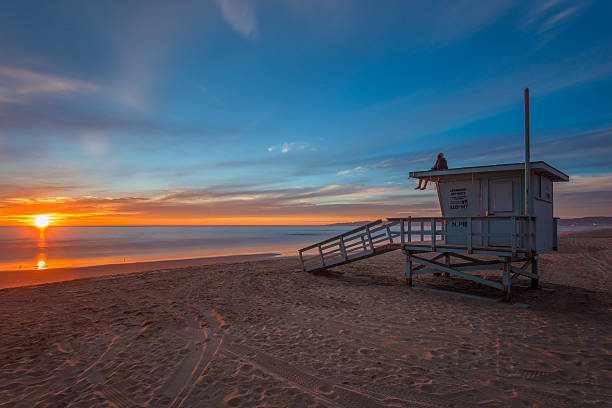 mann sitzt auf der rettungsschwimmer-turm bei sonnenuntergang am strand. - orange county california beach stock-fotos und bilder