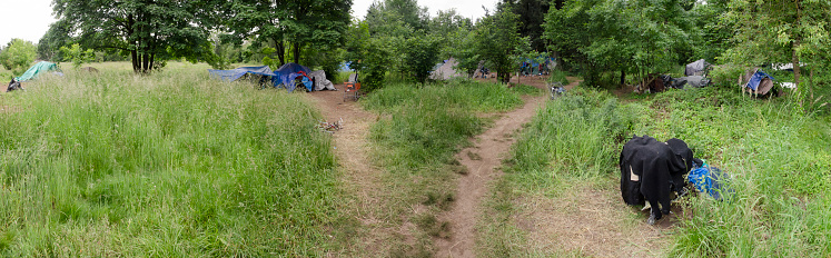 Portland, Oregon, USA-May 26, 2016: Homeless campsites in a field near the Springwater Corridor pedestrian walkway in Southeast Portland, Oregon. One unidentified adult man sits back in the middle of the camp.  The homeless population has become more visible as housing in Portland becomes less affordable.