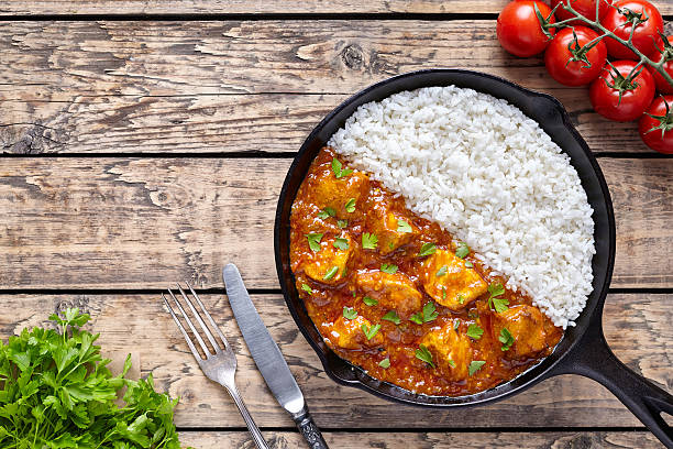 Chicken tikka masala Indian traditional spicy meat food and rice Chicken tikka masala Asian traditional spicy meat food and rice in cast iron skillet with tomatoes, butter, knife. fork and parsley on vintage wooden background. Karahi chicken or korma vindaloo curry powder stock pictures, royalty-free photos & images