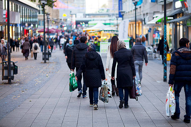 Essen, Germany - October 26, 2015: Rearshot of walking and shopping people with shopping bags in pedestrian zoen Kettwiger Straße of Essen. Women are wearing headscarfs. In background more people are walking.