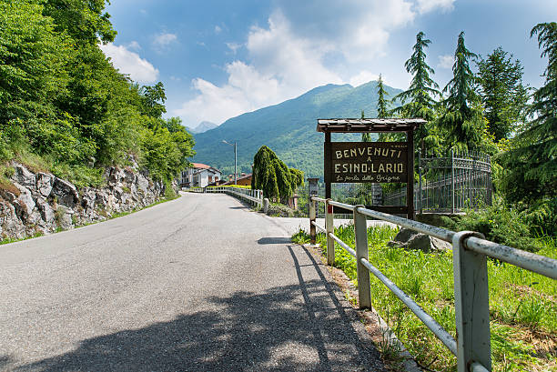 Esino Lario (913 m), Italy, entrance of the village Esino Lario, province of Lecco, Italy - May 27, 2016: tourist sign at the entrance of the village. The sign says: "Welcome to Esino Lario the pearl of the Grigne." Esino Lario, venue between 21 to 28 June 2016 of the 12th international Wikimedia conference, is a small mountain village above Lake Como near Varenna; Grigne are a mountain massif near the village. In the background you can see the first houses of Esino Lario wikipedia stock pictures, royalty-free photos & images