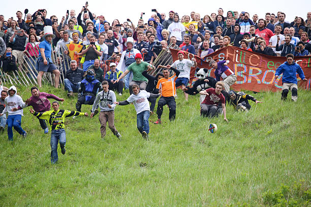 Brockworth, England - May 30, 2016: Entrants chasing the cheese at the 2016 ‘Cheese Rolling’ held at Cooper’s Hill, in the Cotswolds. Every spring bank holiday Monday on the 1 in 2 gradient (Yes 1 in 2!) ‘Coopers Hill’ in the depths of the beautiful Gloucestershire countryside, the slightly ‘More Crazy’ people of not only Gloucestershire but the world gather to pit themselves against ‘The Cheese’. The atmosphere at the event is a true joy with everyone helping each other scale the steep hill. In the true tradition of British stiff upper lip and community spirit a small band of enthusiasts from Brockworth and surrounding area take it upon themselves to organise, control and marshall the event
