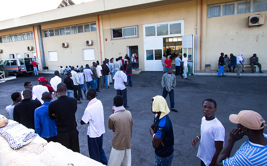 Pozzallo, Sicily, Italy - October 21, 2013: Recent African migrants line up for breakfast in the courtyard of a temporary reception center at the port. Pozzallo is in southern Sicily in Ragusa Province.