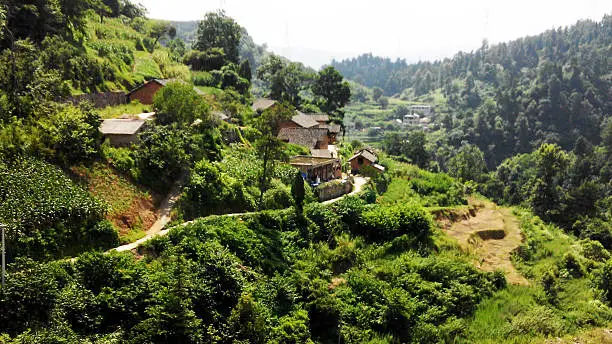 Guiyang Mountains, Guizhou, China - August 7th, 2014: Chinese mountain landscape and tiny quiet  village on the mountainside crossed by the narrow sandy road.