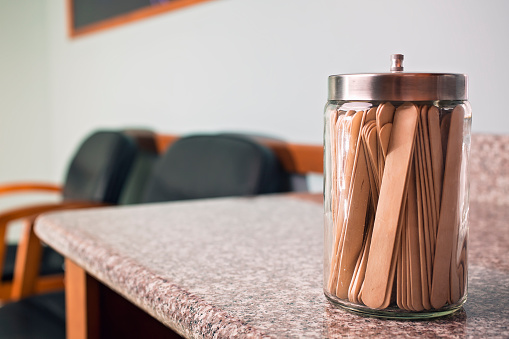 A glass container full of tongue depressors in an exam room