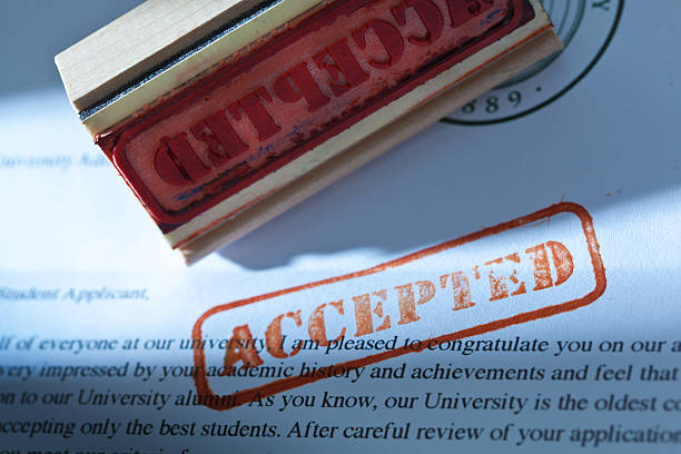 University Application Acceptance Notification Letter with ACCEPTED An acceptance letter from a university application. An university application form and the letter of acceptance with a red rubber stamp of "Accepted" on a table top still life. Photographed close-up in horizontal format with selected focus on the rubber stamp impression. college acceptance letter stock pictures, royalty-free photos & images