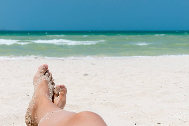 Sandy feet on beach with blurred sea on background stock photo