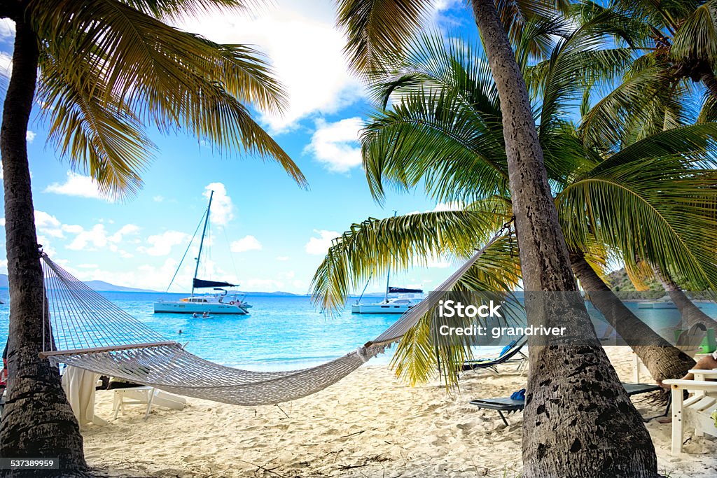 Hammock on the Beach Serene hammock on a quiet beach on a tropical island with sailboat in the bay. Beach Stock Photo