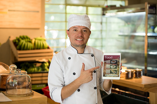 Chef working at a restaurant pointing at the menu on a tablet computer and smiling. Design on tablet is own design.