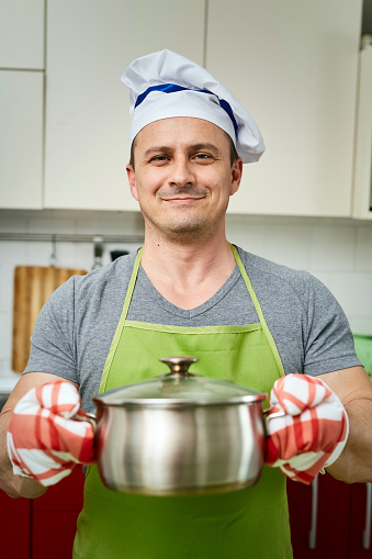 Handsome cook holding a stainless steel pot with lid on