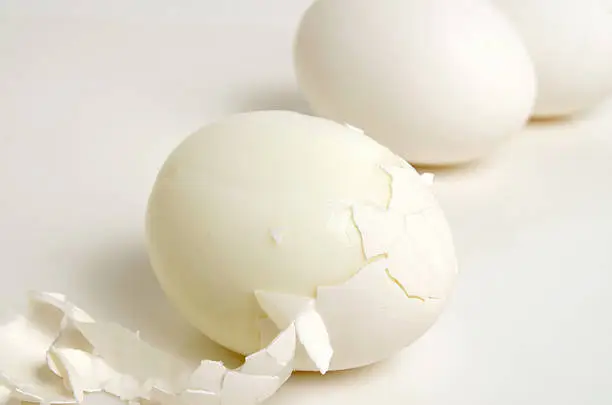 Cleaning the boiled egg from the shell, on a light background, close up.