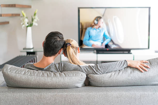 Loving couple watching tv at home Happy couple relaxing at home watching tv and holding the remote control. Release of Model on TV is also attached. couch back stock pictures, royalty-free photos & images